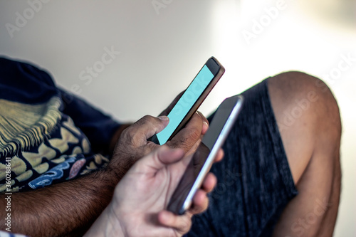 Unrecognizable group of young people using mobile phone at home. Couple sitting of sofa and sending text message on their mobiles. Close-up of couple holding mobile phones in hands.