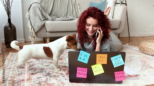 Young attractive woman tlking on the phone and playing with her pet. Woman typing on the laptop. Lady and her dog indoor. photo