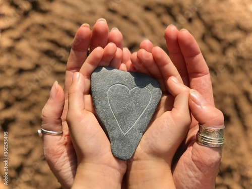 Mother and Daughter holding a love heart stone at the beach on beautiful summers day