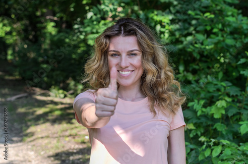 Young charming girl in summer park shows like sign with hand