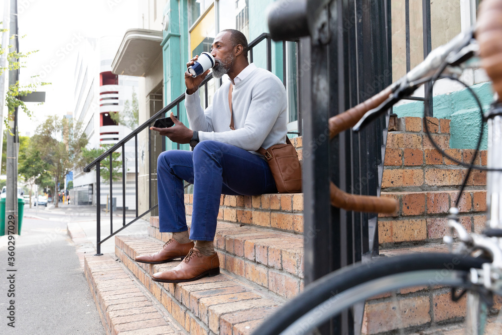 African American man sitting on stairs and drinking a takeaway coffee African American man sitting on stairs and drinking a takeaway coffee