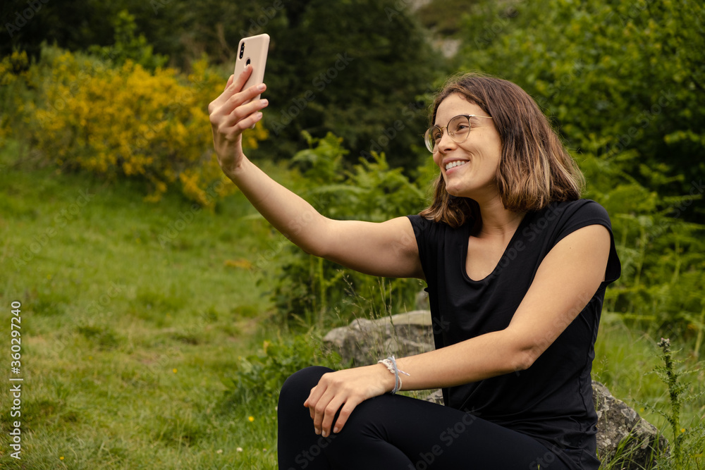 Young woman sat taking a selfie with her mobile phone after a hike in the nature Young woman sat taking a selfie with her mobile phone after a hike in the nature