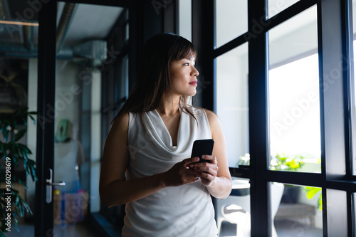 Asian woman looking outside and holding her phone