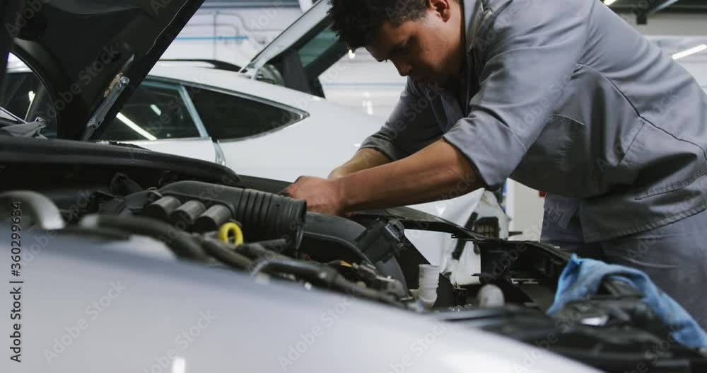 African American male car mechanic looking at an open car engine and checking if something is broken African American male car mechanic looking at an open car engine and checking if something is broken