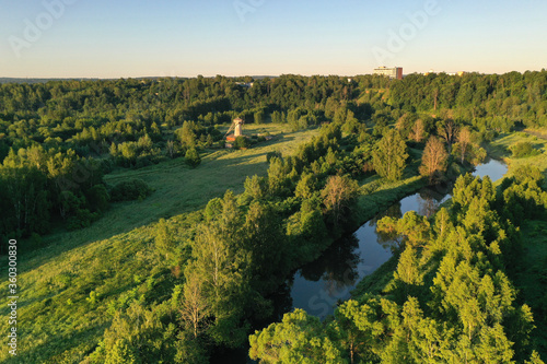 Fototapeta Naklejka Na Ścianę i Meble -  panoramic view of green meadows a large wooden mill in the morning haze at sunrise shot from a drone at dawn