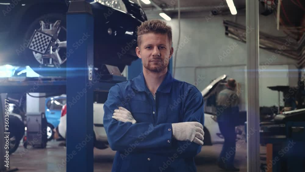 portrait of a car mechanic at work at the car repair shop, smiling man at factory warehouse with flares