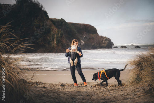 A woman with an infant is playing with a dog on the Californian beach photo
