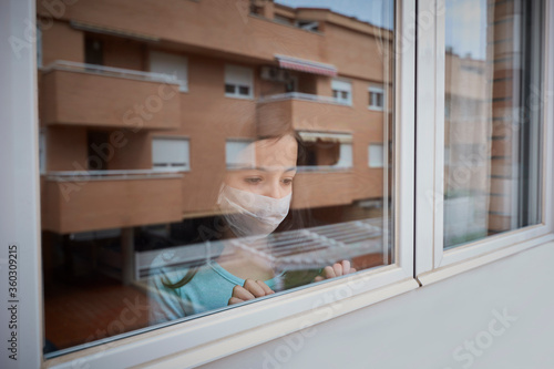 Girl with face mask looking out the window quarantined by covid-19 photo