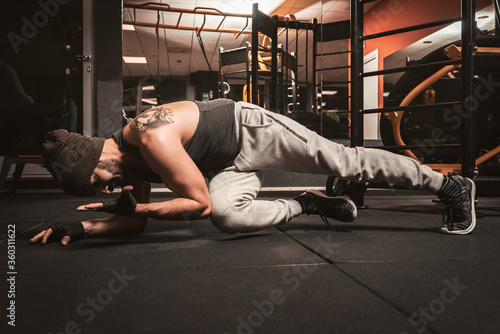 Fototapeta Naklejka Na Ścianę i Meble -  A sporty man in the gym is doing Yoga exercises. Push up alternative exercises. Plank with Knee to Elbow Exercise. Yoga mental benefits.