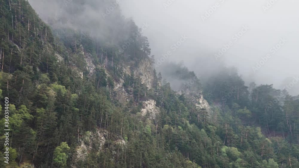 timelapse steep mountain slopes covered with coniferous pine forest with sharp rocks. Low clouds cling to trees in cloudy weather with precipitation. timelapse steep mountain slopes covered with coniferous pine forest with sharp rocks. Low clouds cling to trees in cloudy weather with precipitation.
