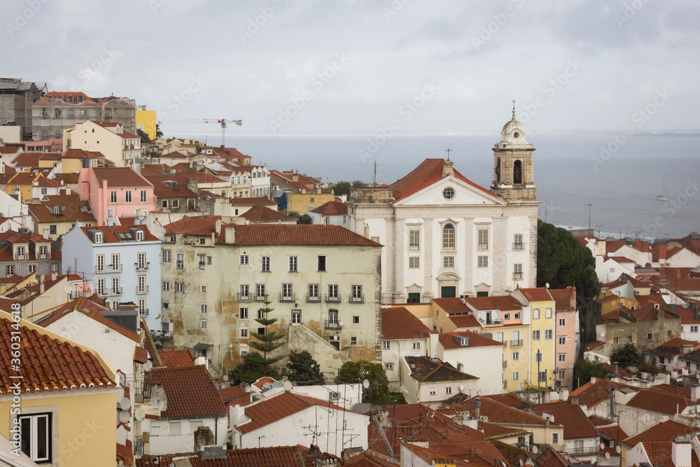 Great views of Alfama district with sea on background on cloudy day in Lisbon. Colorful houses and church in Portugal capital. Traditional old town architecture concept