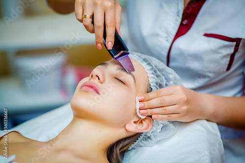 Woman receiving ultrasonic facial exfoliation at cosmetology salon. Procedure clearing clogged pores, ultrasonic treatment for skin rejuvenation, beautician uses modern apparatus for refreshing © Maxim