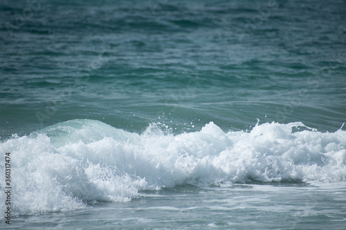 Small cresting wave in the Atlantic Ocean on the coast. Blue green ocean waves with sea foam and salt water spray. Beach travel photos.