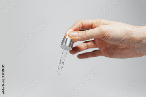 Close-up of female hand holding a pipette with cosmetic essential oil for skin care. Studio background of grey color with copy space.