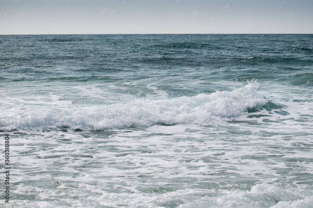 Small cresting wave in the Atlantic Ocean on the coast. Blue green ocean waves with sea foam and salt water spray. Beach travel photos.