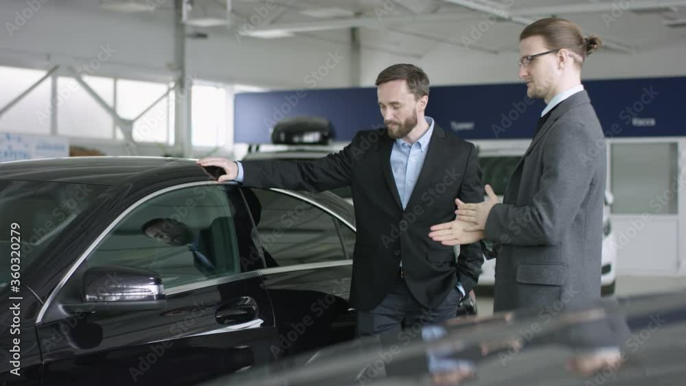 Trader discussing automobile purchase with businessman in dealership. Auto dealer is working with his customer at the dealership showing a new automobile. Trader discussing automobile purchase with businessman in dealership. Auto dealer is working with his customer at the dealership showing a new automobile.