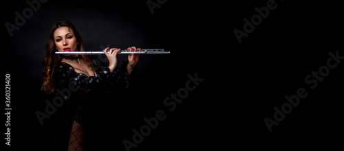 Female girl artist in suit with flute on black background. Flute in hand. Player with orchestra music instrument. Isolated on black. Author's space. Large background space for an inscription or logo