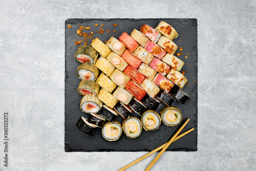 Fresh fish sushi set with side dishes on a black graphite board and gray background