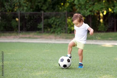 Toddler boy stopping soccer ball at football field. Little football player with raised leg ready to kick ball back in game. Young athlete and active childhood concept. Copy space