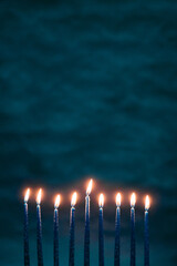 Burning blue candles on a Jewish menorah at Hanukkah with a dreidel on a dark blue background