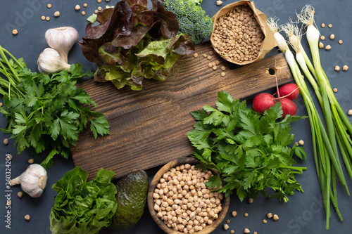 Green vegetables and lentils and chickpeas peas lie around a rustic of wooden cutting board. Place for text. Cooking healthy bio food in the kitchen at home. Salad Ingredients