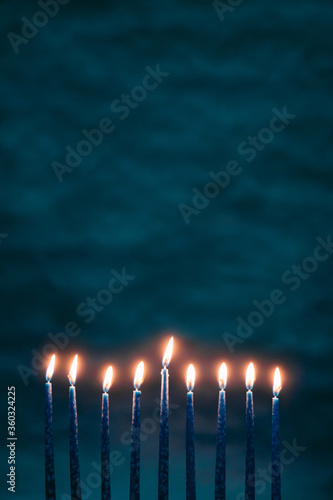 Burning blue candles on a Jewish menorah at Hanukkah with a dreidel on a dark blue background photo