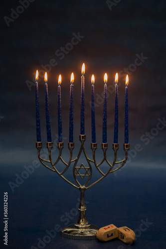 Cuadro en lienzo Burning blue candles on a Jewish menorah at Hanukkah with a dreidel on a dark bl
