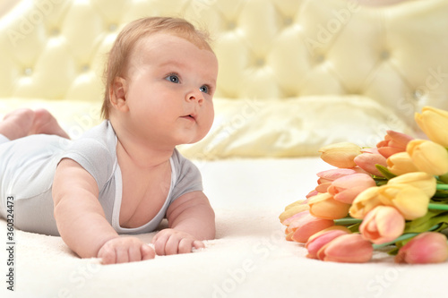 Cute little baby girl with flowers on bed