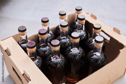 Full glass bottles with a cork cap are placed in a cardboard box. Dark liquid in a bottle, on a light background