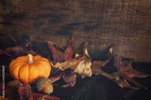 Fotografia, Obraz a dark rustic wood table filled with fall leaves and a bright orange miniature p