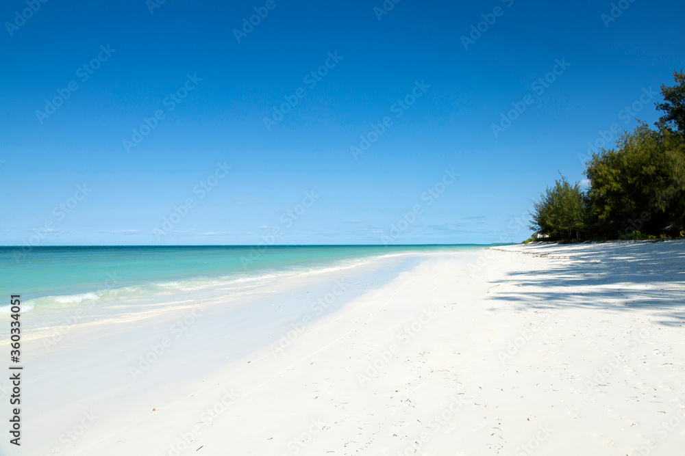 Fototapeta premium Czysta plaża z białym piaskiem z turkusową wodą. Tle tropikalnej wyspy. Małe fale miażdżące na plaży. Czysta pusta plaża z białym piaskiem na Zanzibarze.