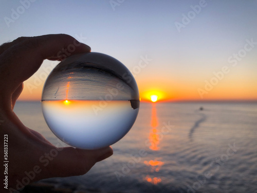 Φωτογραφία Woman's hand holding a crystal ball, looking through to sea and sky at dawn