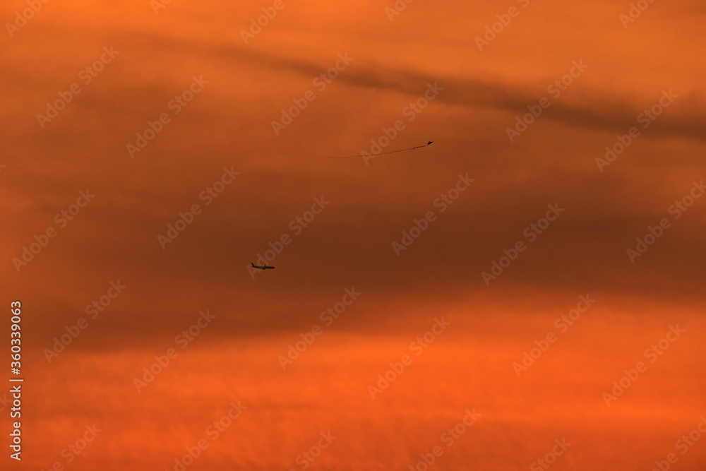silhouettes of an airplane and a kite, which appear to be on the same plane, flying under an orange sky during dusk.