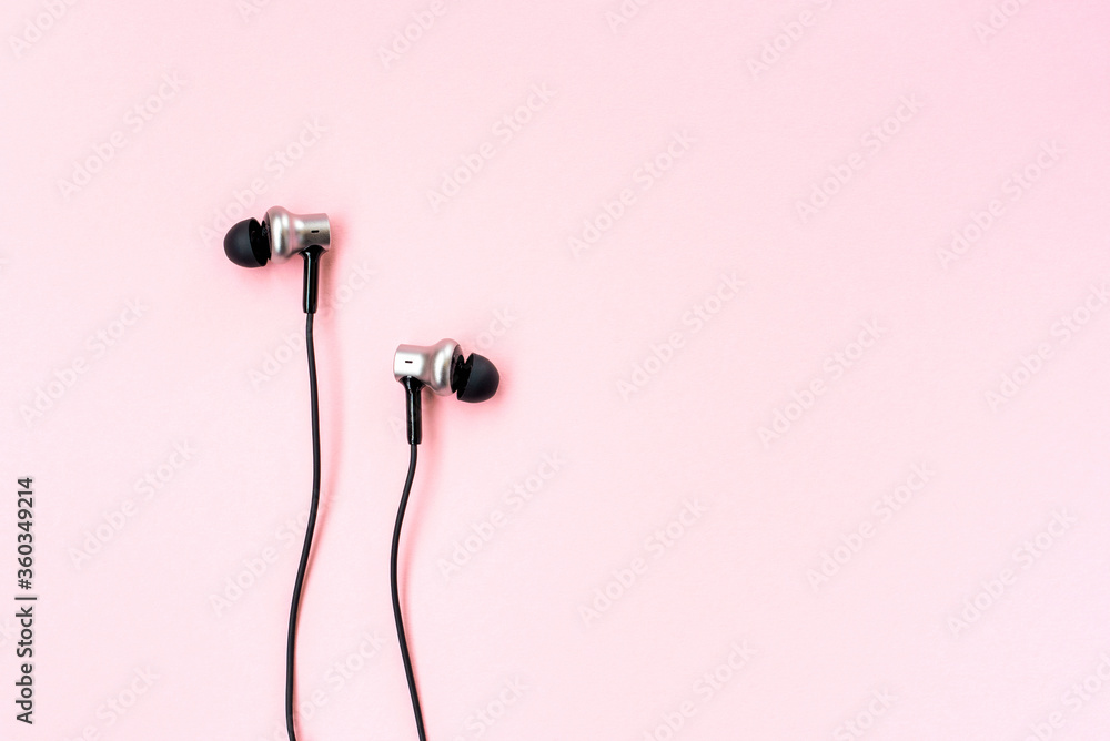 Black music earphones for smartphone on a pink pastel background. Minimalist flat lay. Empty place for writing. Copy space. Top closeup view. Black music earphones for smartphone on a pink pastel background. Minimalist flat lay. Empty place for writing. Copy space. Top closeup view.
