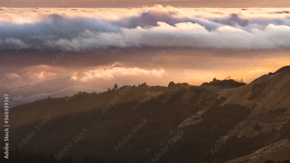 Sunset landscape in Santa Cruz mountains with sunlight illuminating a valley covered by a blanket of clouds; San Francisco Bay Area, California