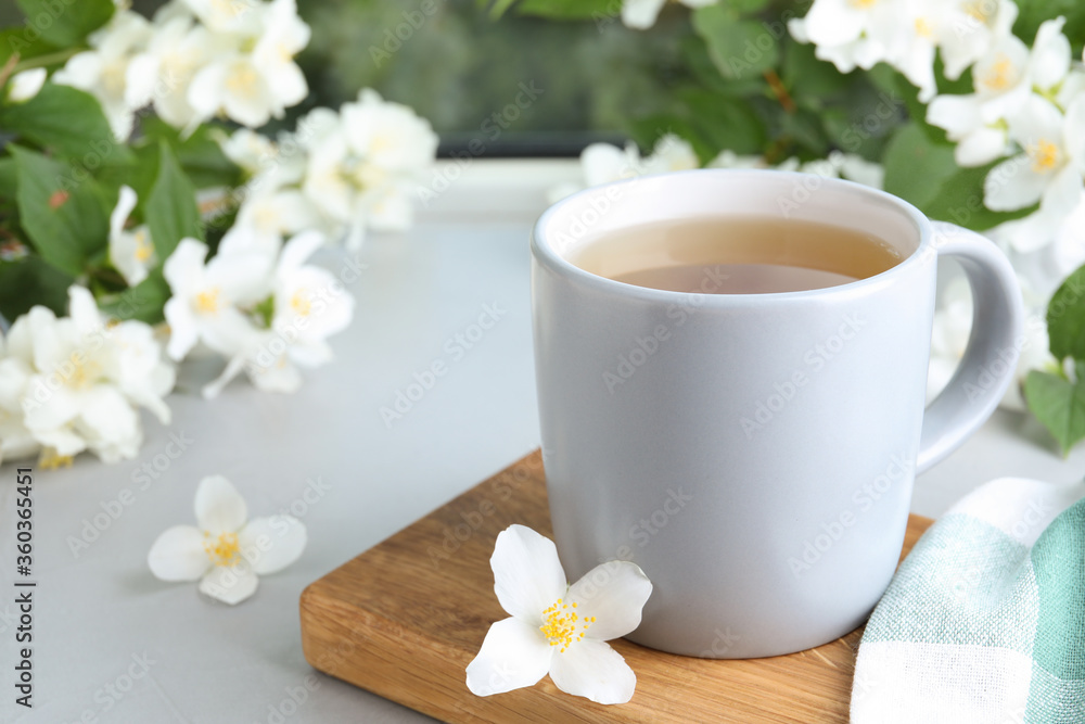Cup of tea and fresh jasmine flowers on light grey table. Space for text