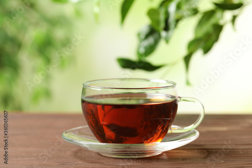 Cup of black tea on wooden table against blurred background. Space for text