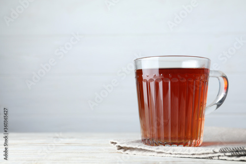 Glass cup of aromatic black tea on white wooden table, space for text