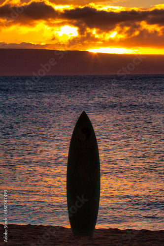 Silhouetted surfboard planted in the sand at sunset on Maui.