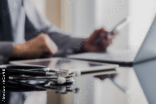 Blurred image of doctor man working on computer and using mobile smart phone.