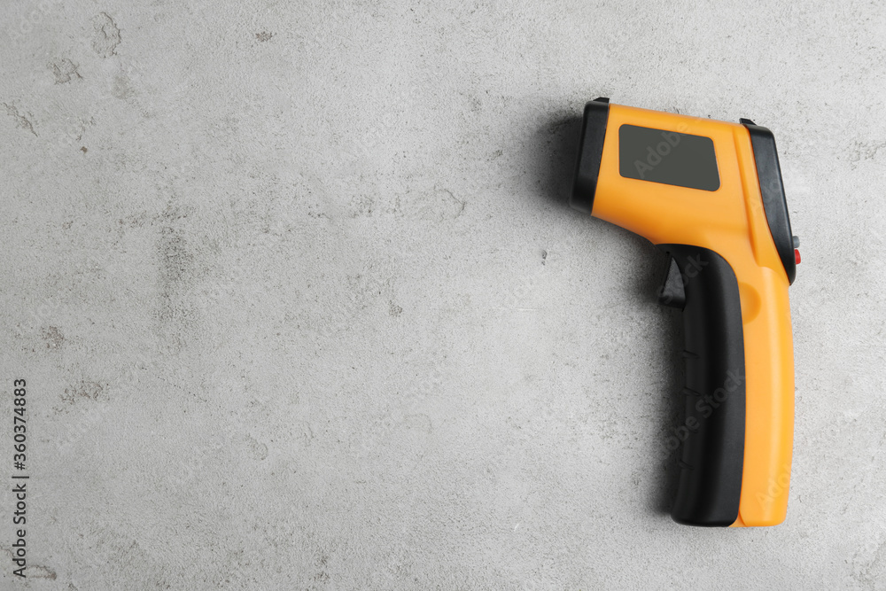 Modern non-contact infrared thermometer on light grey stone background, top view. Space for text