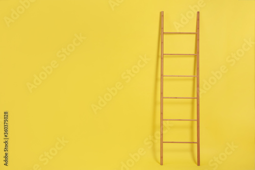 Modern wooden ladder on yellow background. Space for text
