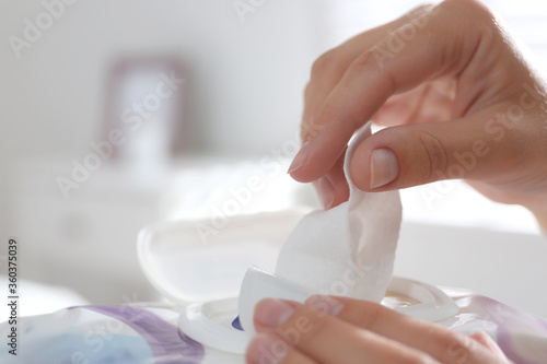 Woman taking wet wipe out of pack against blurred background, closeup