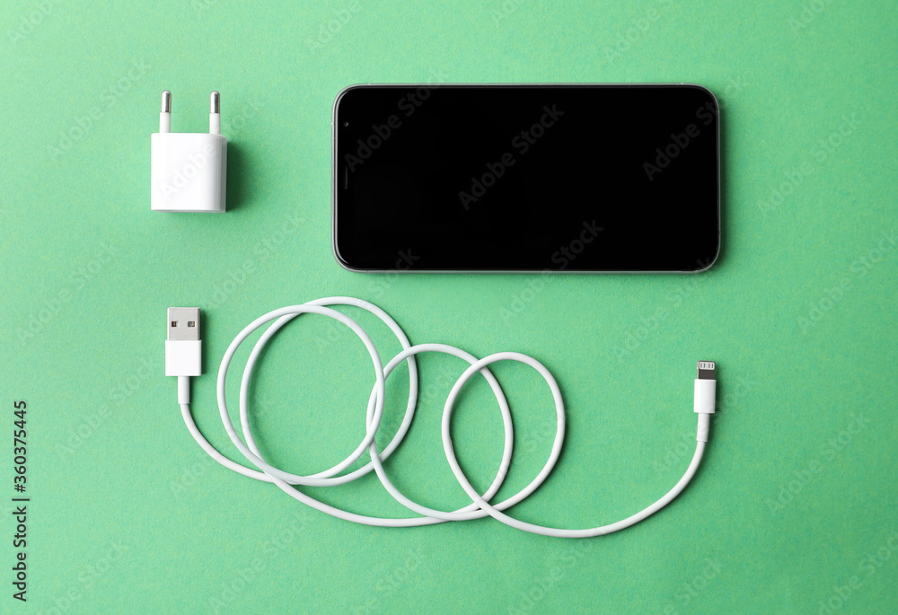 Smartphone and USB charger on green background, flat lay. Modern technology Smartphone and USB charger on green background, flat lay. Modern technology