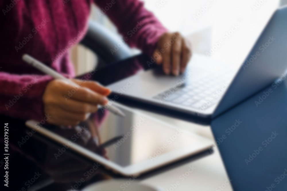 Blurred image of business woman hands using electronic or stylus pen and work on white digital tablet pc with laptop computer on the desk at modern home office. Work from home, online learning concept Blurred image of business woman hands using electronic or stylus pen and work on white digital tablet pc with laptop computer on the desk at modern home office. Work from home, online learning concept