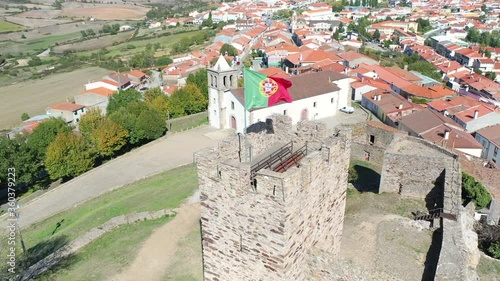 (flying around a POI) Portuguese flag on the castle tower and a cityscape of Mogadouro town, district of Braganca, Tras-os-Montes, Portugal photo