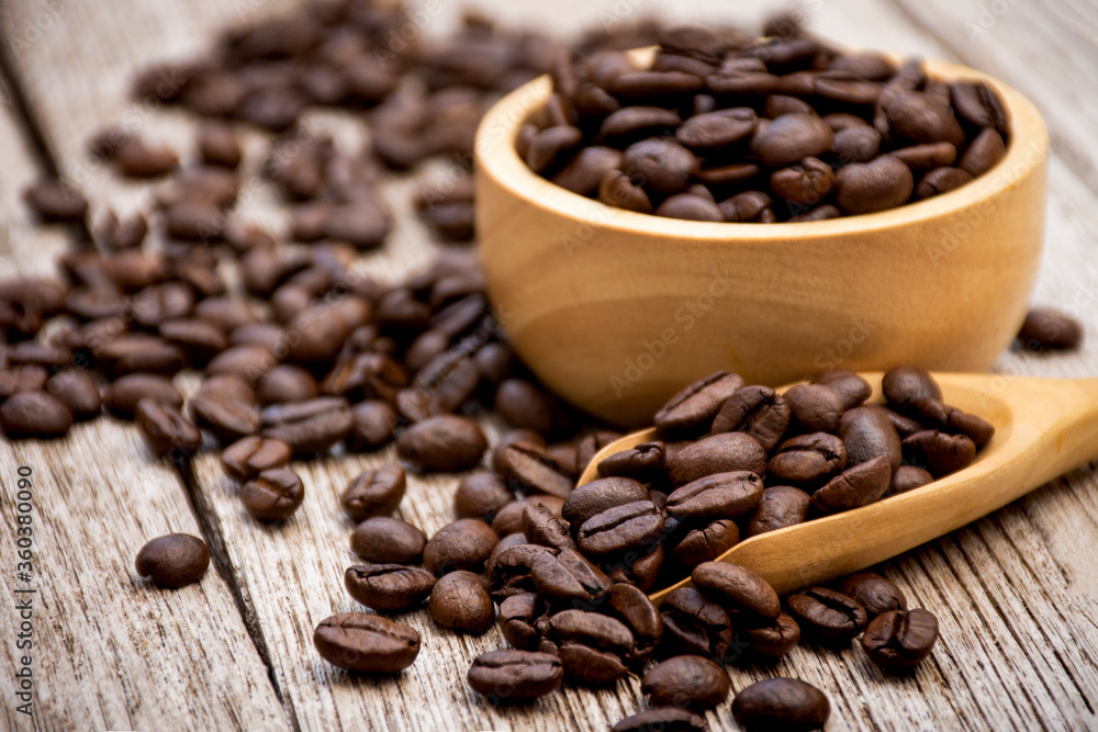 coffee beans in a wooden scoop and bowl on wooden table.