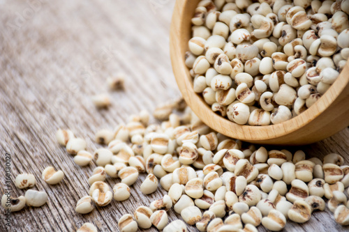 White Job's tears ( Adlay millet, pearl millet or coix seeds ) in wooden bowl  isolated on wood table background. 