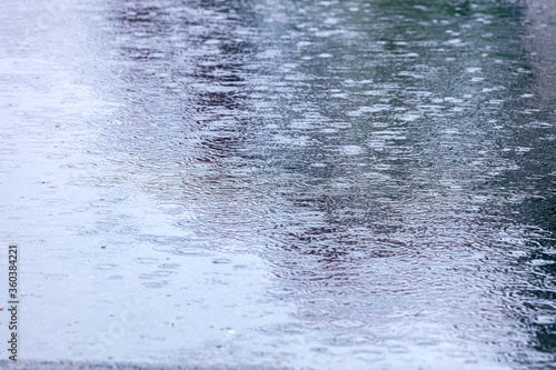 heavy rain with multiple splashes and circles on the surface of large city puddle