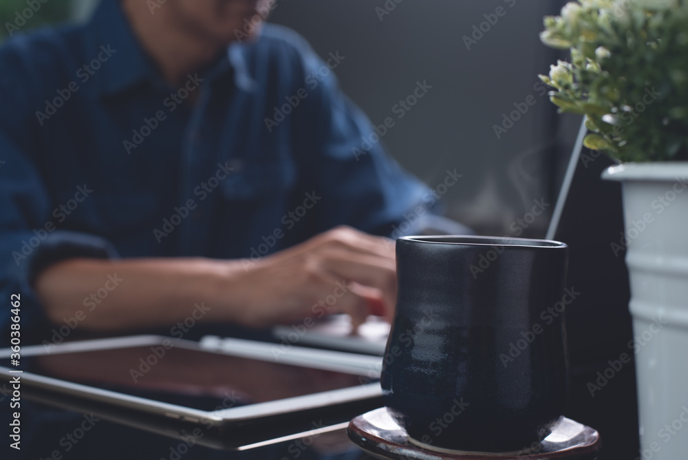 Man online working on laptop computer at night at home office with cup of hot coffee on table Man online working on laptop computer at night at home office with cup of hot coffee on table